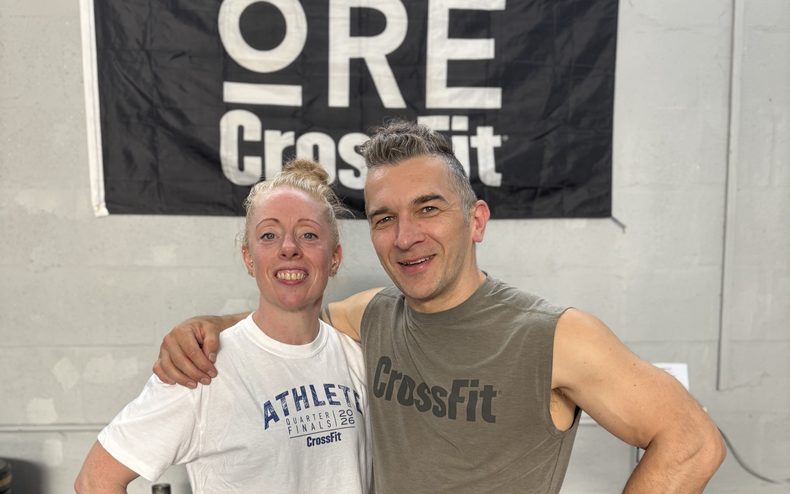 Coaches Vic and Adam, both 50, smiling in front of the ORE CrossFit banner